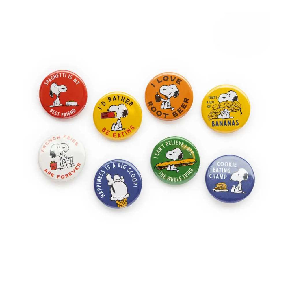 A collection of colorful button pins with Peanuts characters, including Snoopy, and various food items like bananas and peanuts.